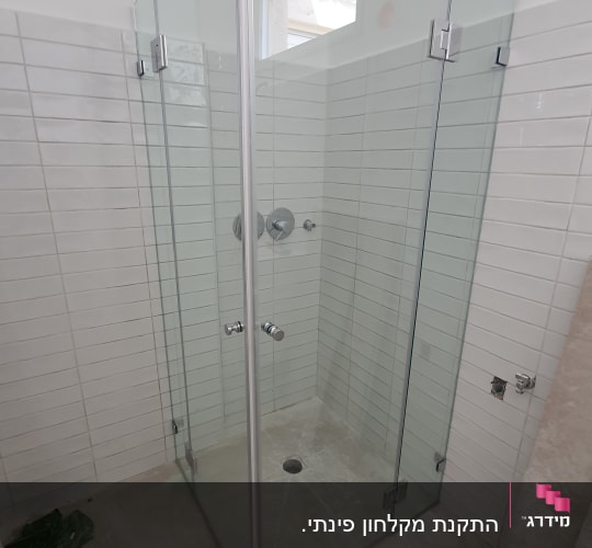 מקלחון זכוכית עם אריחים לבנים וברזי מתכת